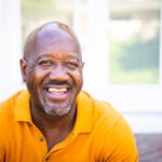 a mature black man looks out while standing on his porch